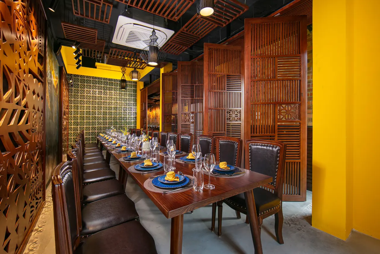 Long dining table beside carved wooden doors and a yellow wall