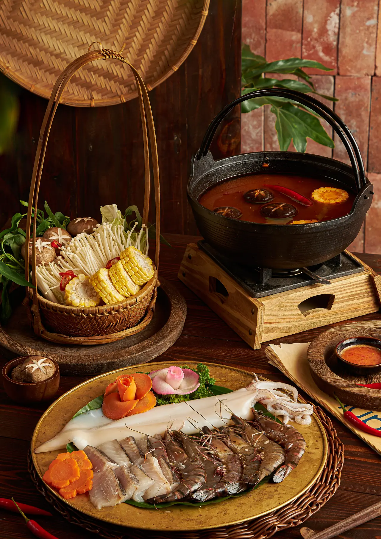 Hot pot on a stove with a platter of fish, prawns and squid and a basket of mushrooms