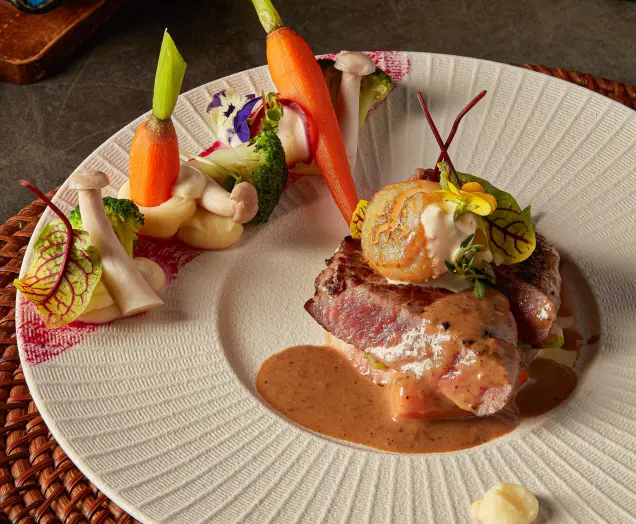 Pan-seared beef with scallop and baby vegetables on a white plate